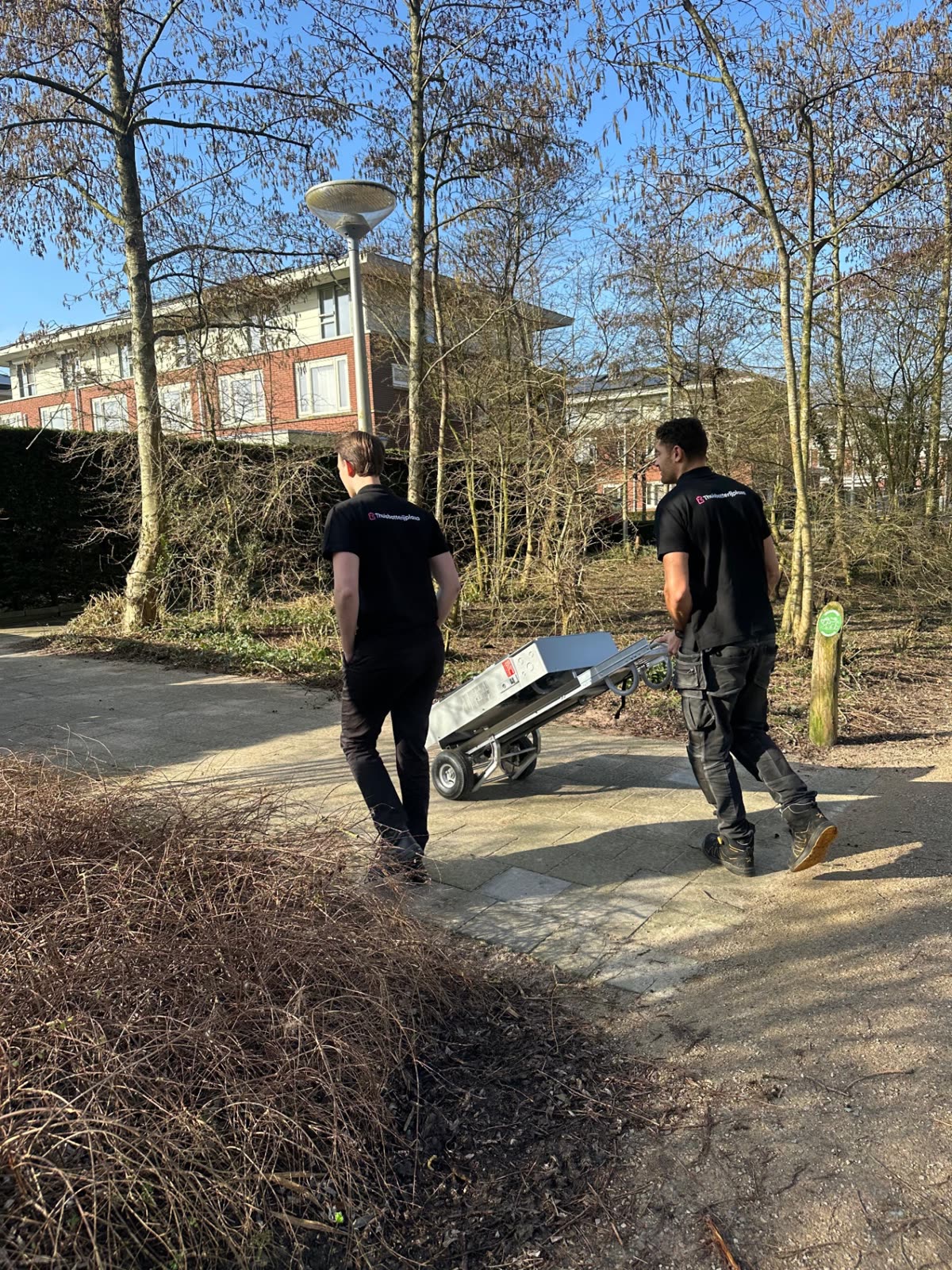 Twee monteurs brengen een thuisbatterij met een steekkar naar de woning