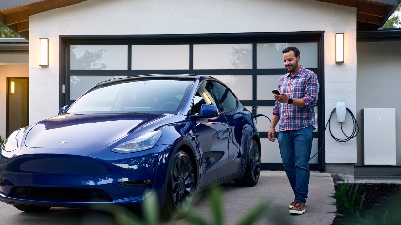 Bewoner bekijkt de Tesla-app bij een Powerwall, laadpaal en elektrische auto voor slim energiemanagement — Slim energiemanagement: haal meer uit uw zonnepanelen