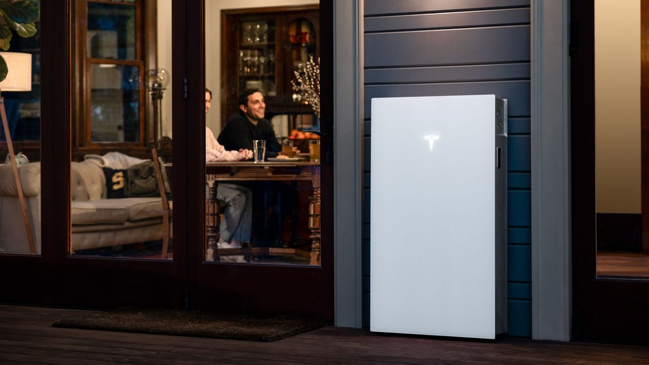 Tesla Powerwall 3 aan de gevel terwijl bewoners binnen goedkope stroom van een dynamisch contract gebruiken — Tesla Powerwall met een dynamisch energiecontract: zo werkt het