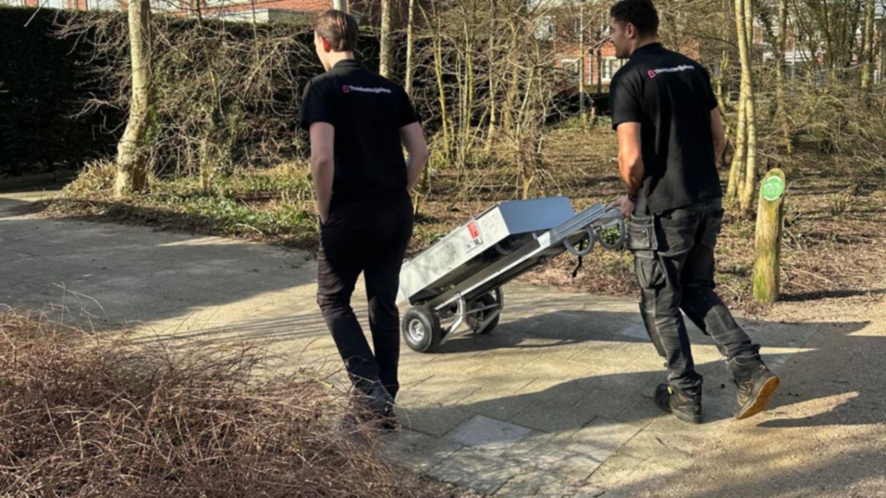 Twee monteurs van Thuisbatterijplaza vervoeren een Tesla Powerwall op een steekkar