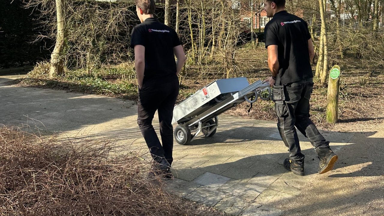 Gecertificeerde monteurs brengen een Tesla Powerwall met een steekkar naar de woning voor installatie — Thuisbatterij installeren: het complete stappenplan